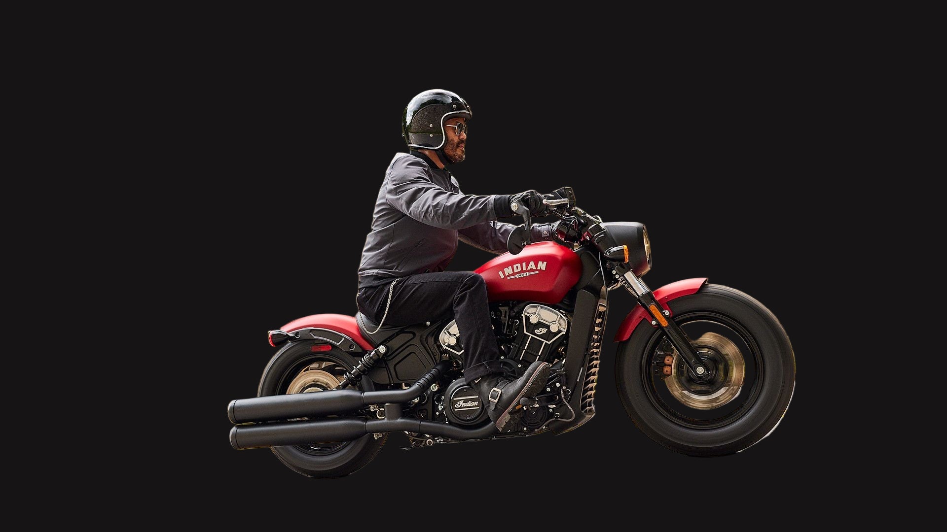 Person riding a red motorcycle on a road with a stone wall and greenery in the background