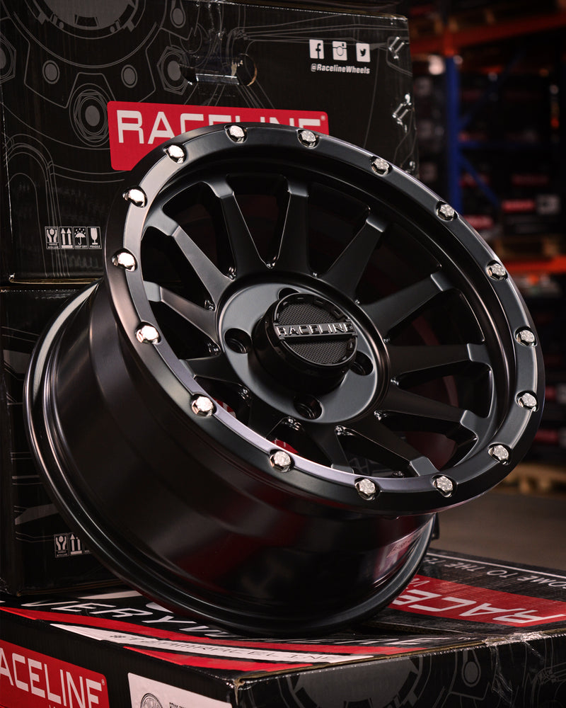 Black alloy wheel on a box with 'RaceLine' branding in a warehouse setting