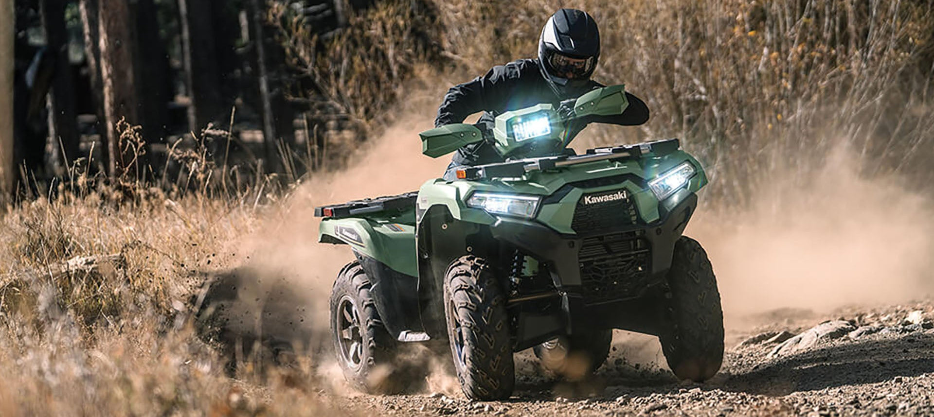 Person riding a green Kawasaki ATV through a forested area